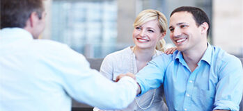 Smiling young couple shaking hands with their property consultant